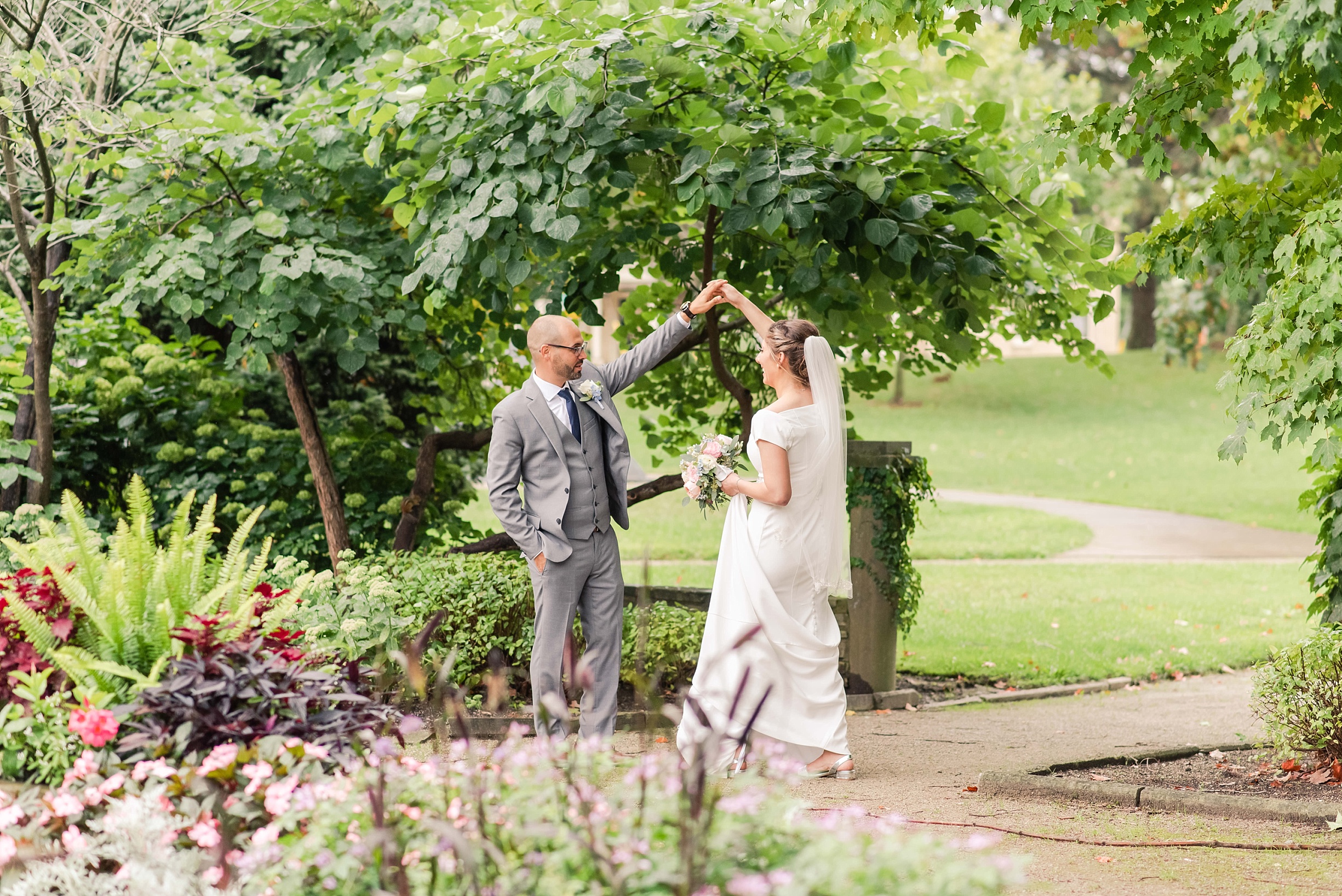 a groom in a grey suit twirls a bride around with her arm above her head. used in a blog post about wedding day timelines.