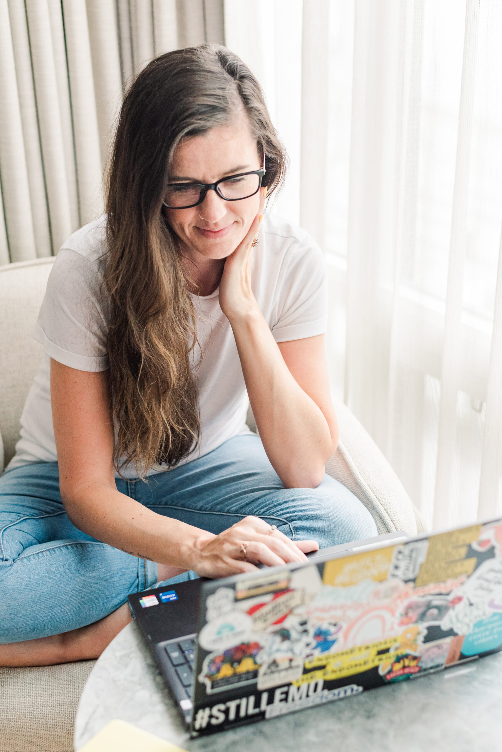 london ontario wedding photographer sandra henderson works at her laptop by a window with her hand resting on her neck