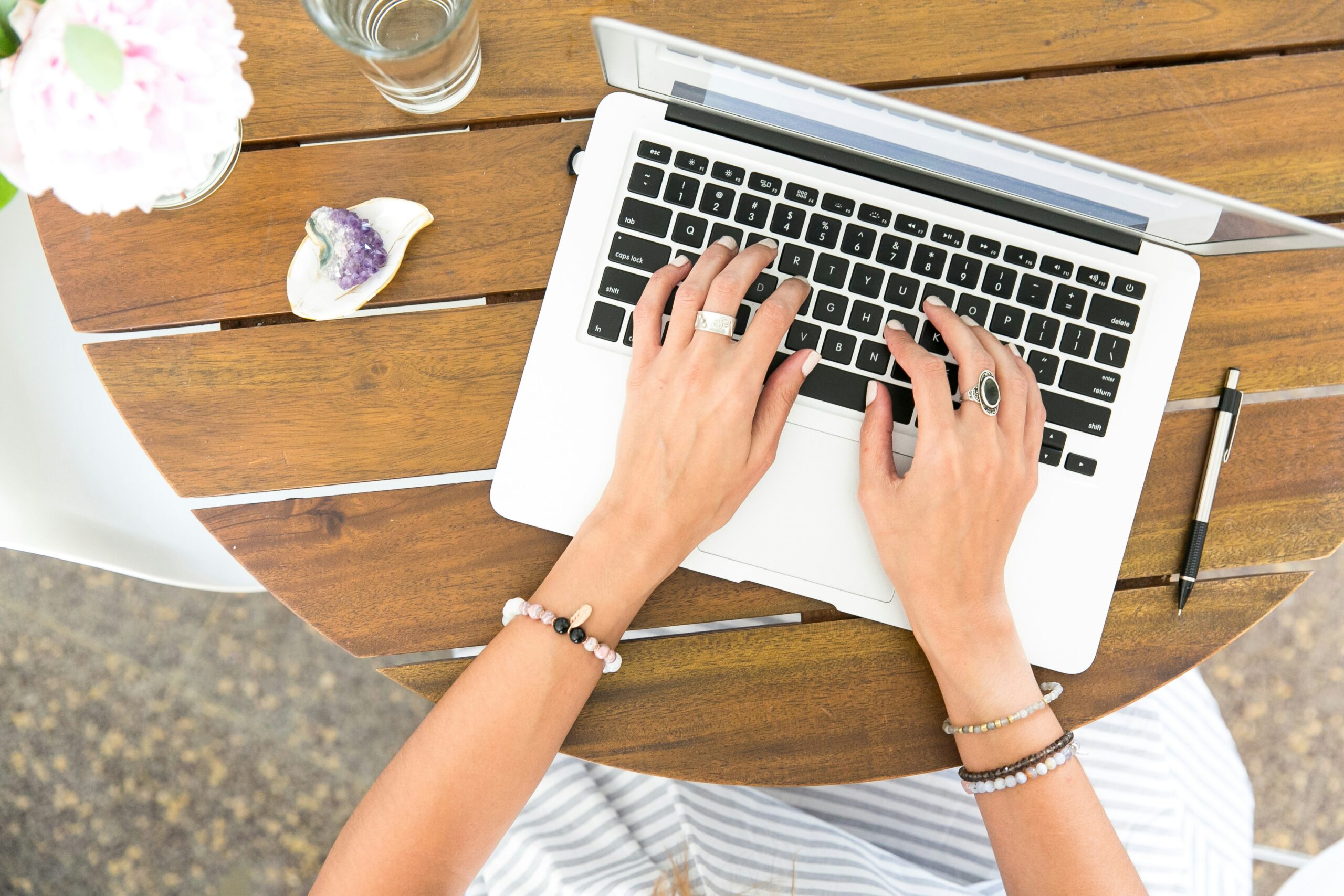 a woman's hands type on a laptop set on a wooden table. photo is used in a blog post about creating a photography locations gallery.