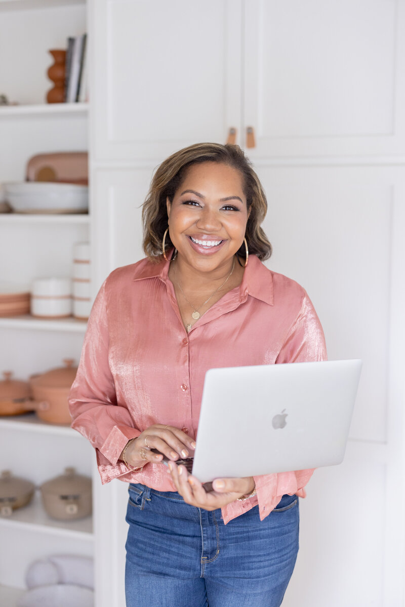 A photo of Angie McPherson smiling at the camera while holding a laptop