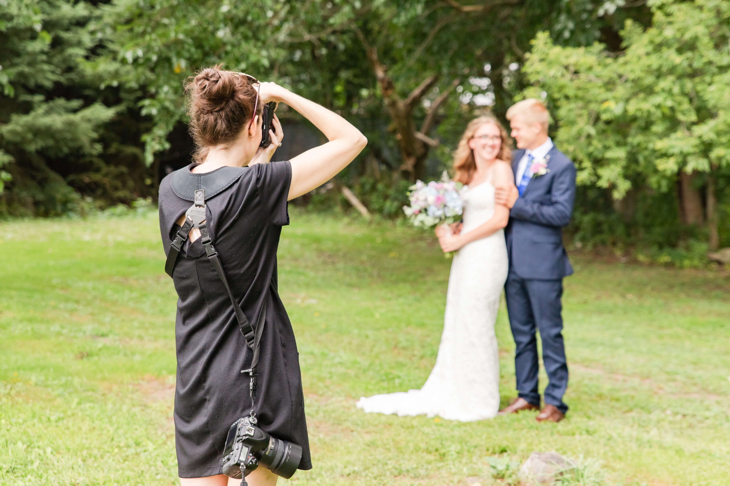 Wedding photographer taking pictures of a couple outdoors, representing the demanding behind-the-scenes work that can lead to wedding photographer burnout.
