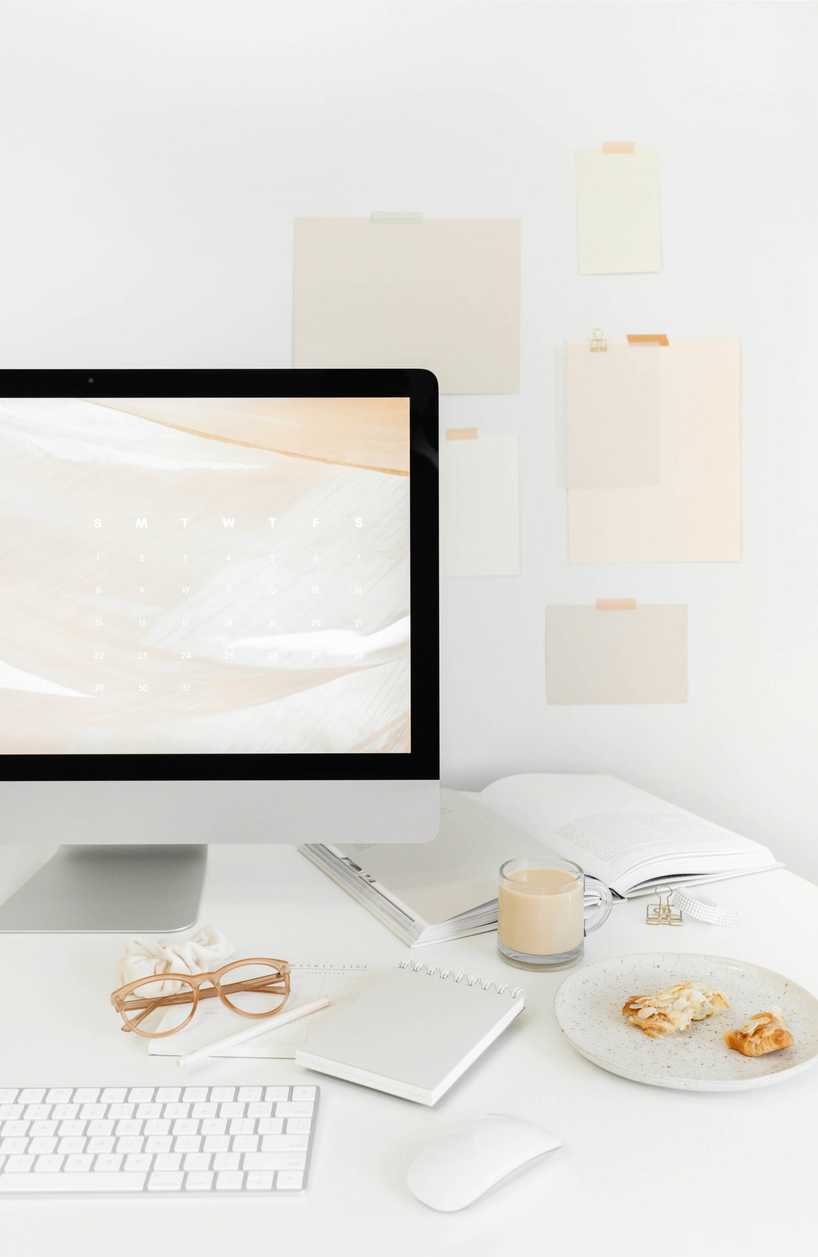Minimal white desk with a computer, glasses, notebook, keyboard, and coffee, styled stock photo used for a blog about wedding photographer burnout.