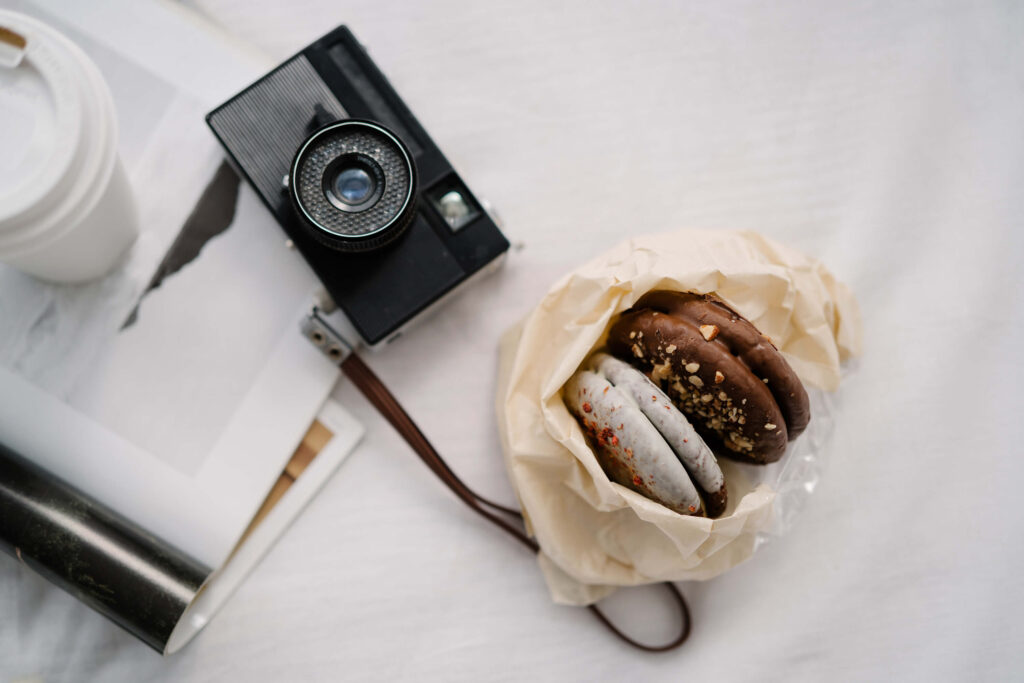 A flatlay of a vintage camera, coffee cup, and wrapped cookies on a white background, styled for a wedding photographer working on email marketing with Flodesk.