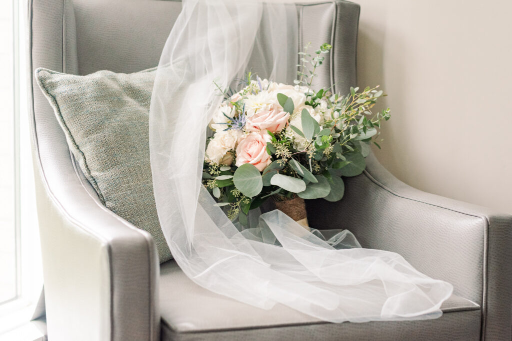 a bouquet and a veil rest on a grey leather chair