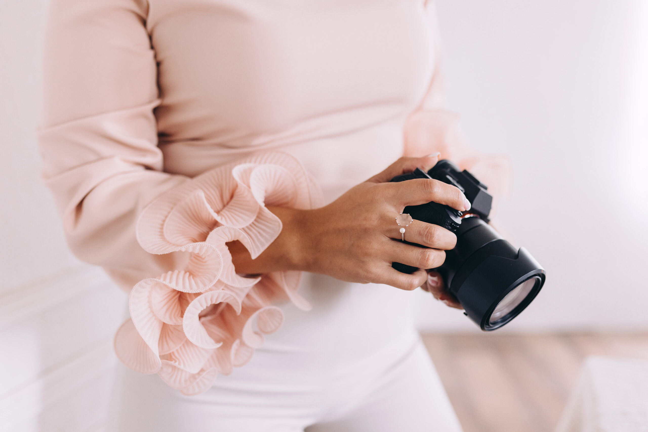 A woman in a light pink shirt is holding her camera around waist-level. Used in a blog post about photography business organization