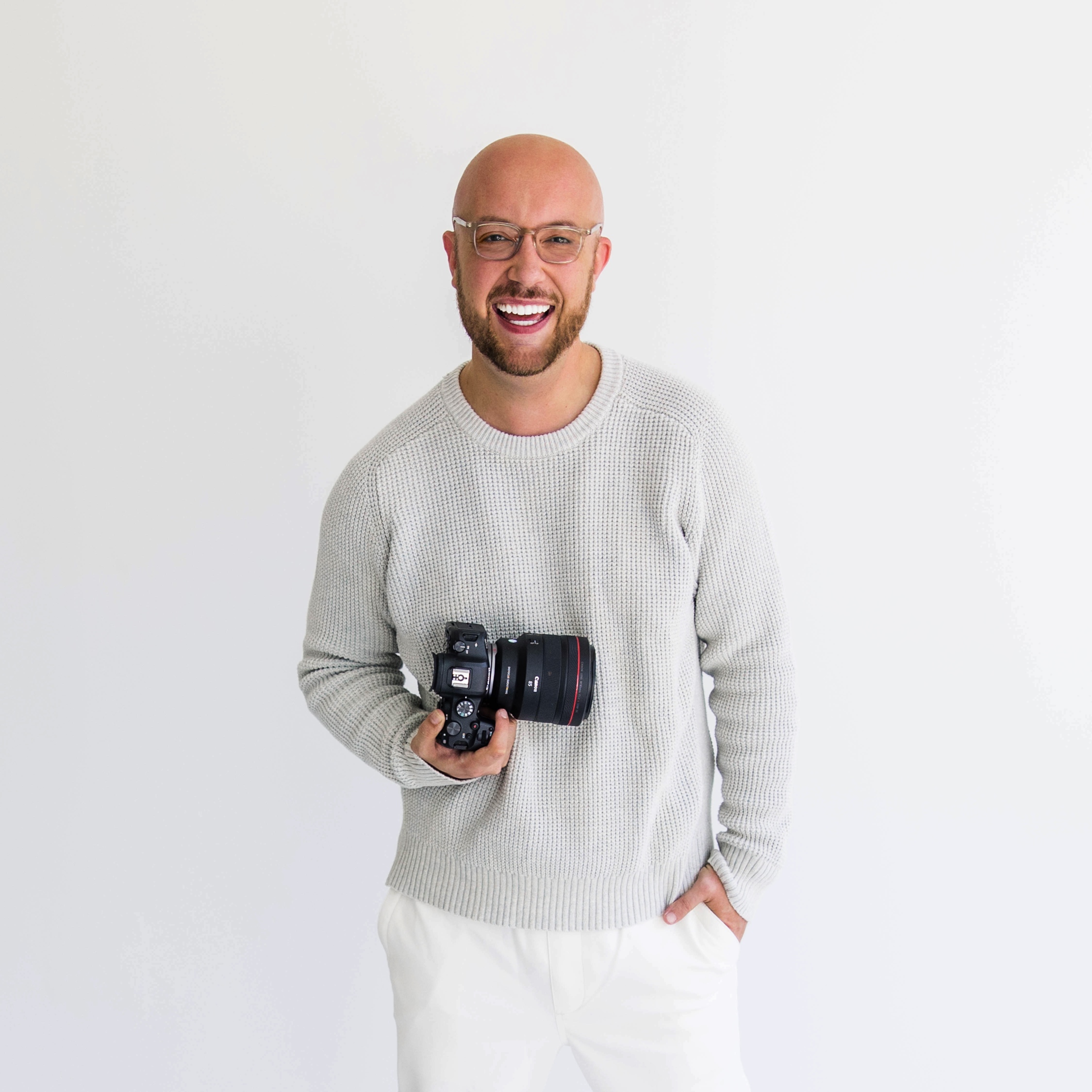 rob from square 8 studios stands holding a camera and smiling in front of a white background