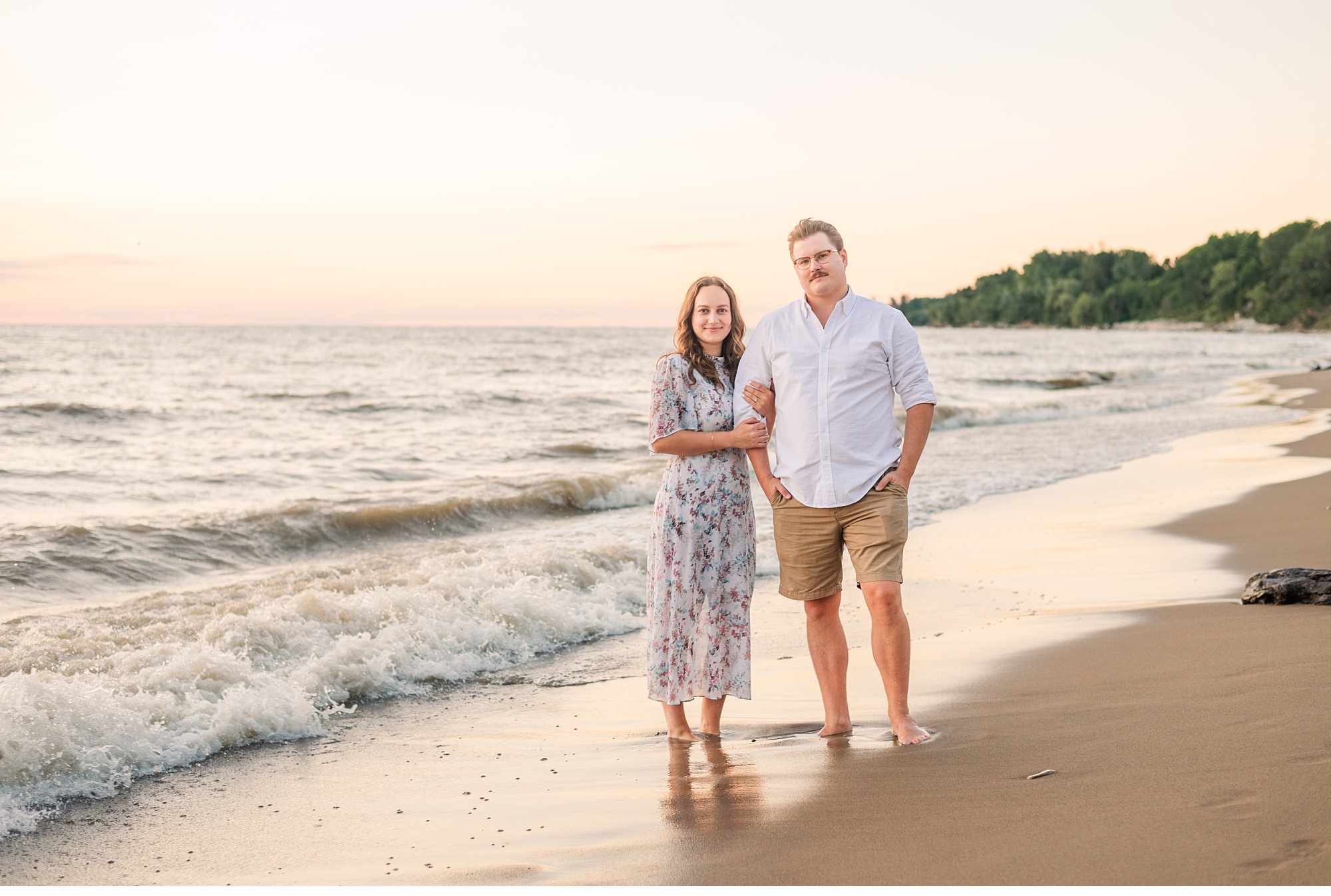 a couple stands on the beach at sunset with waves splashing at their feet. Used as a cover photo in a wedding photography education blog post.