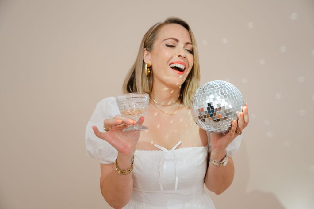 A smiling woman in a white dress holding a glass and a disco ball, representing celebration and sustainability in email marketing for wedding photographers.