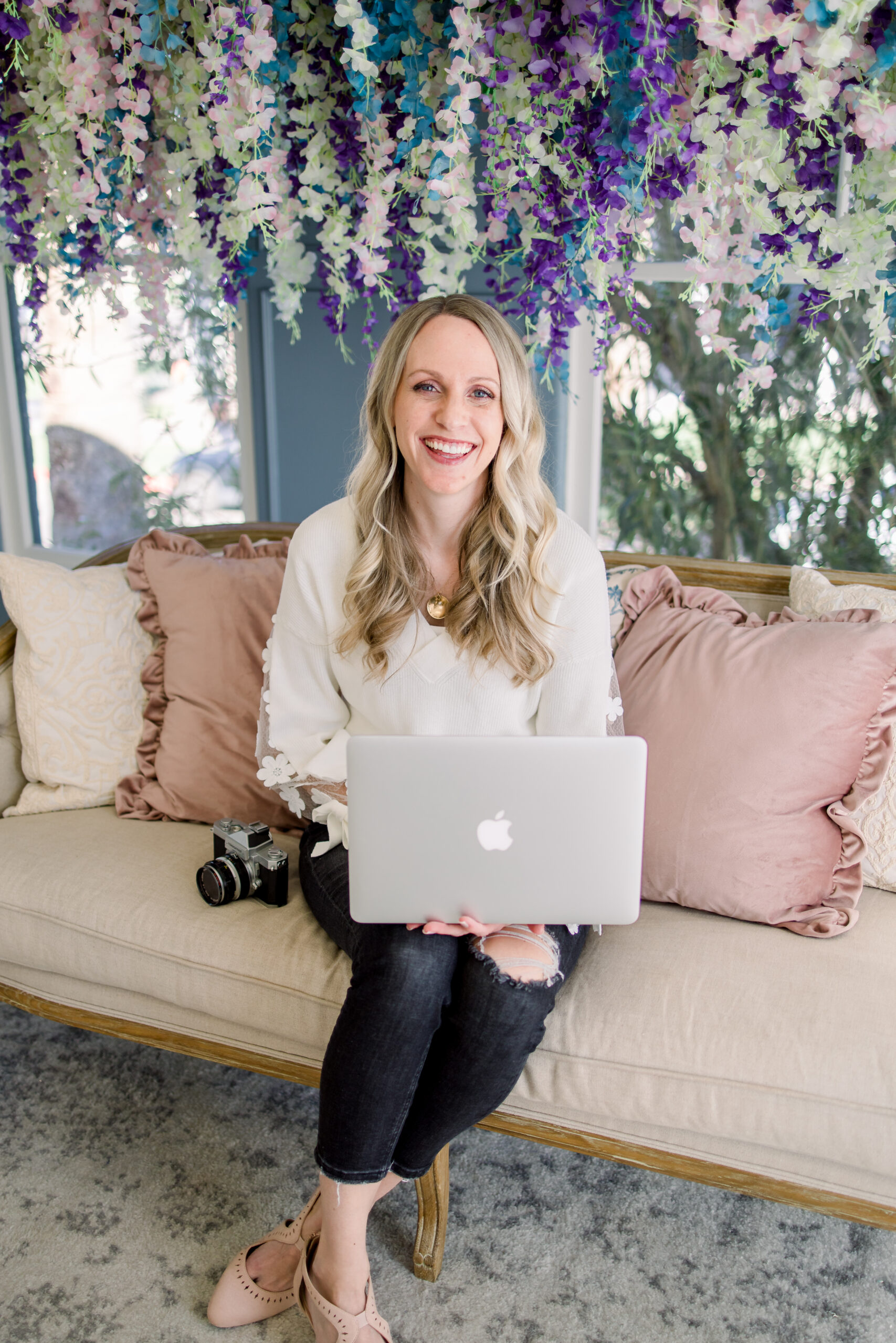 janelle joy photo editing sits on a couch with a laptop on her lap. used in a blog post about how to outsource photo editing