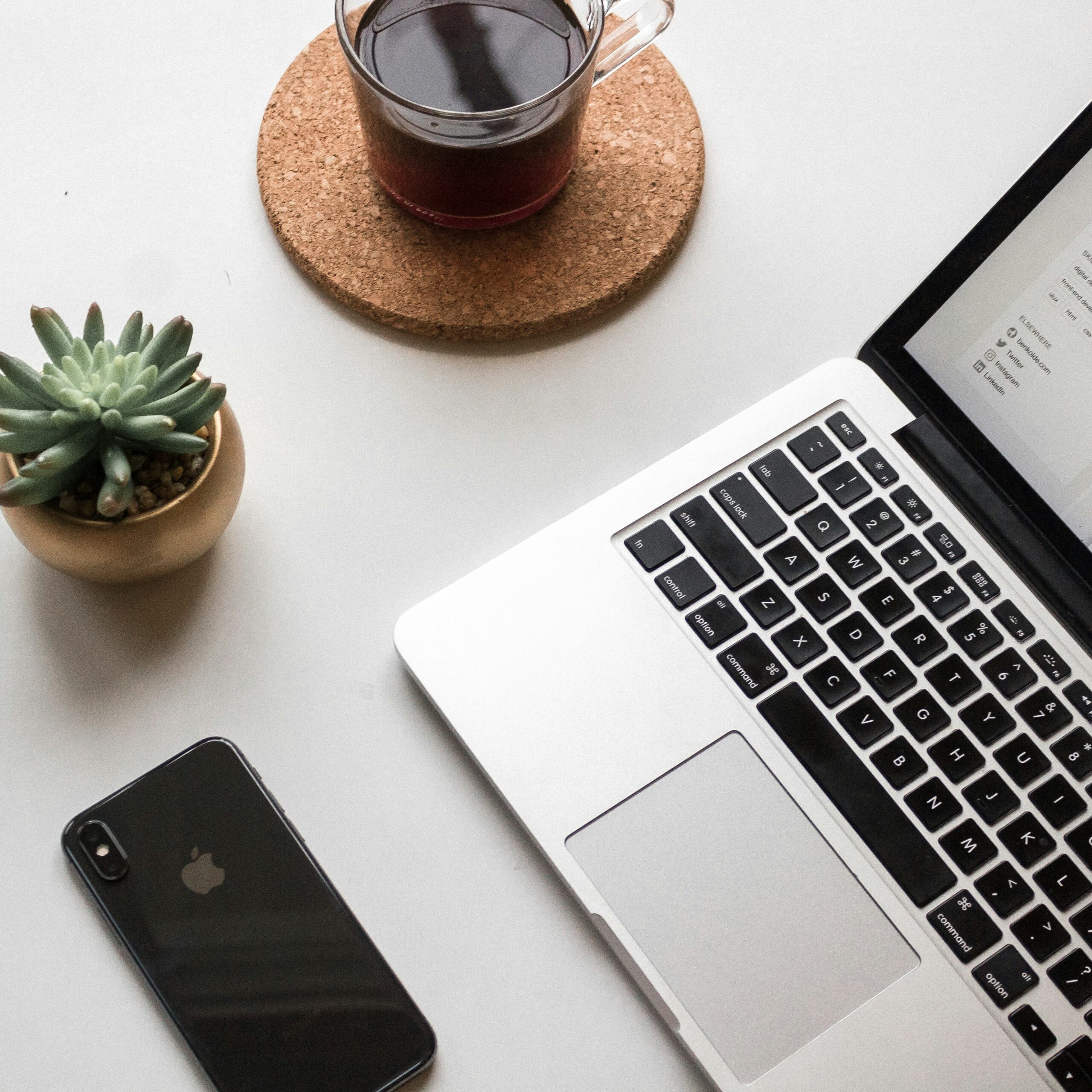a laptop, a phone, a cup of coffee, and a succulent on a white table. used in a blog post about using pic-time to increase your photography print sales.