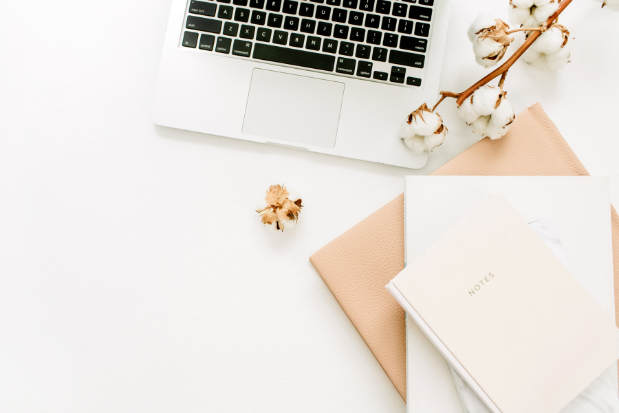 A laptop on a white table, with notebooks in the bottom right corner, and a stick of cotton placed on top for aesthetics. used in a blog post comparing honeybook vs dubsado for wedding photographers and family photographers