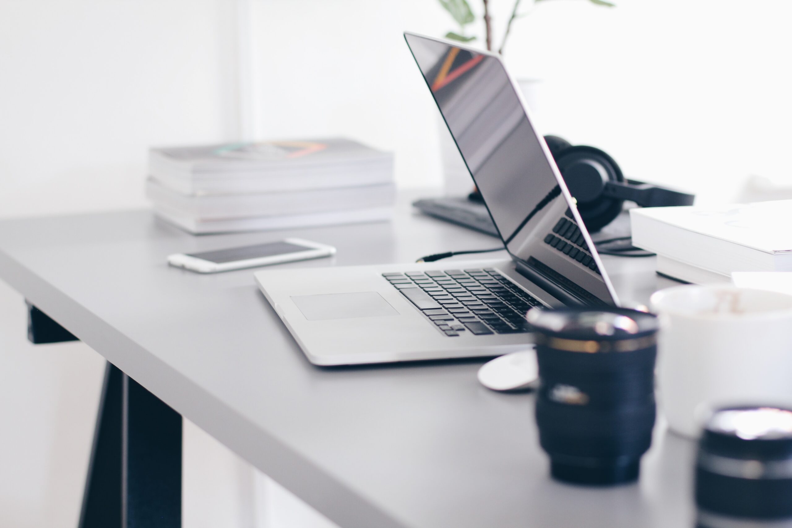 a laptop and a camera lens on a desk. photo used in a blog post about essential tools for engagement season