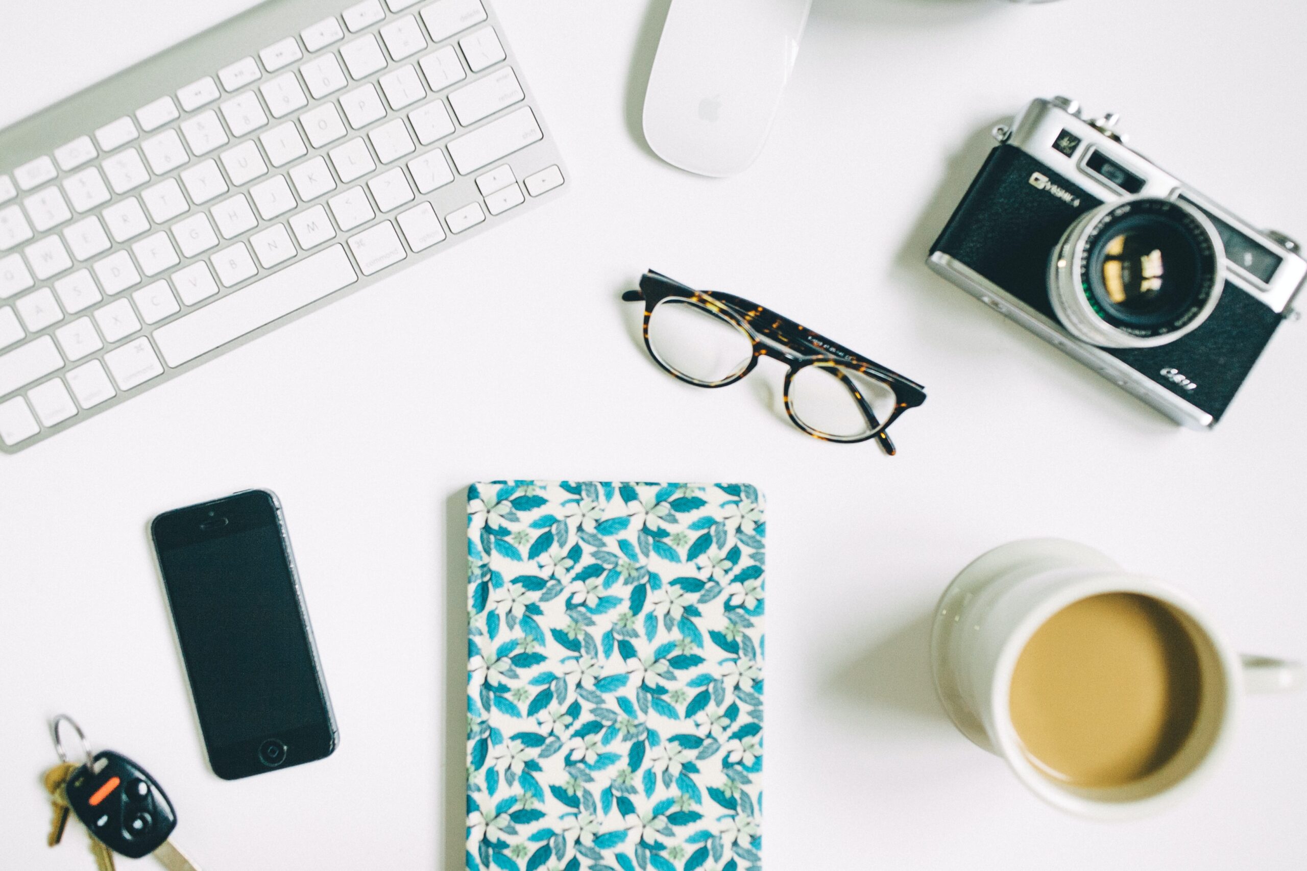 a notebook, glasses, camera, and keyboard on a desk, used in a blog post about how to book more weddings