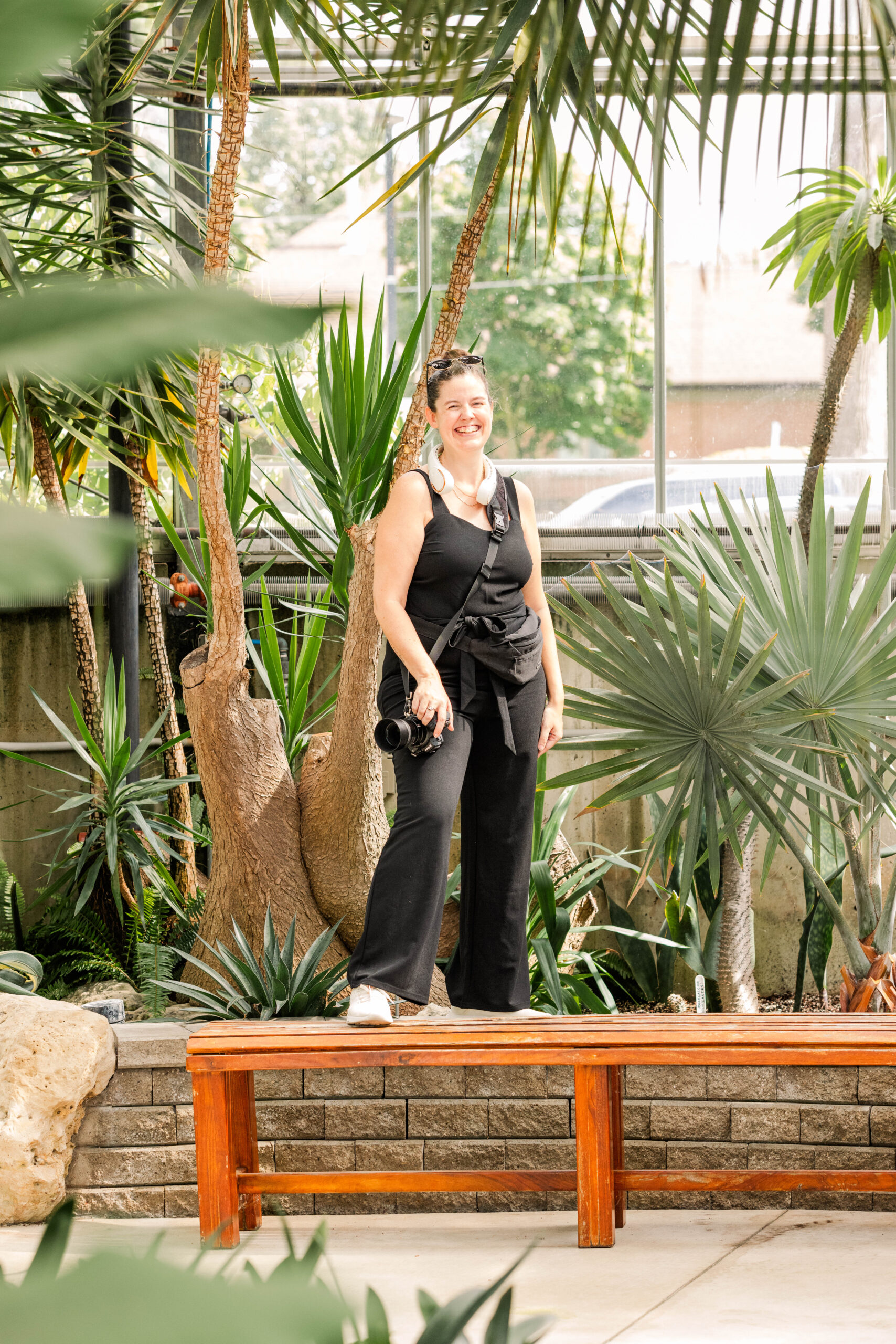 sandra stands on a bench in a greenhouse while holding her camera