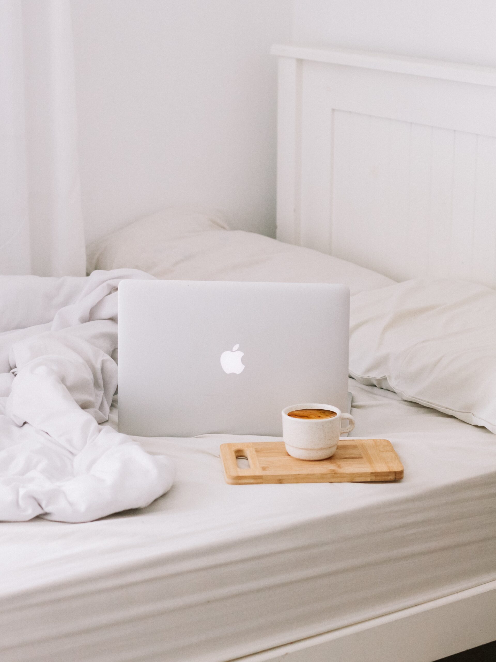 a laptop and cup of coffee on a tray both sit on a bed with white sheets and a white blanket. used in a blog post called How I Built a Wedding Day Timeline System as a Photographer with a Chronic Illness