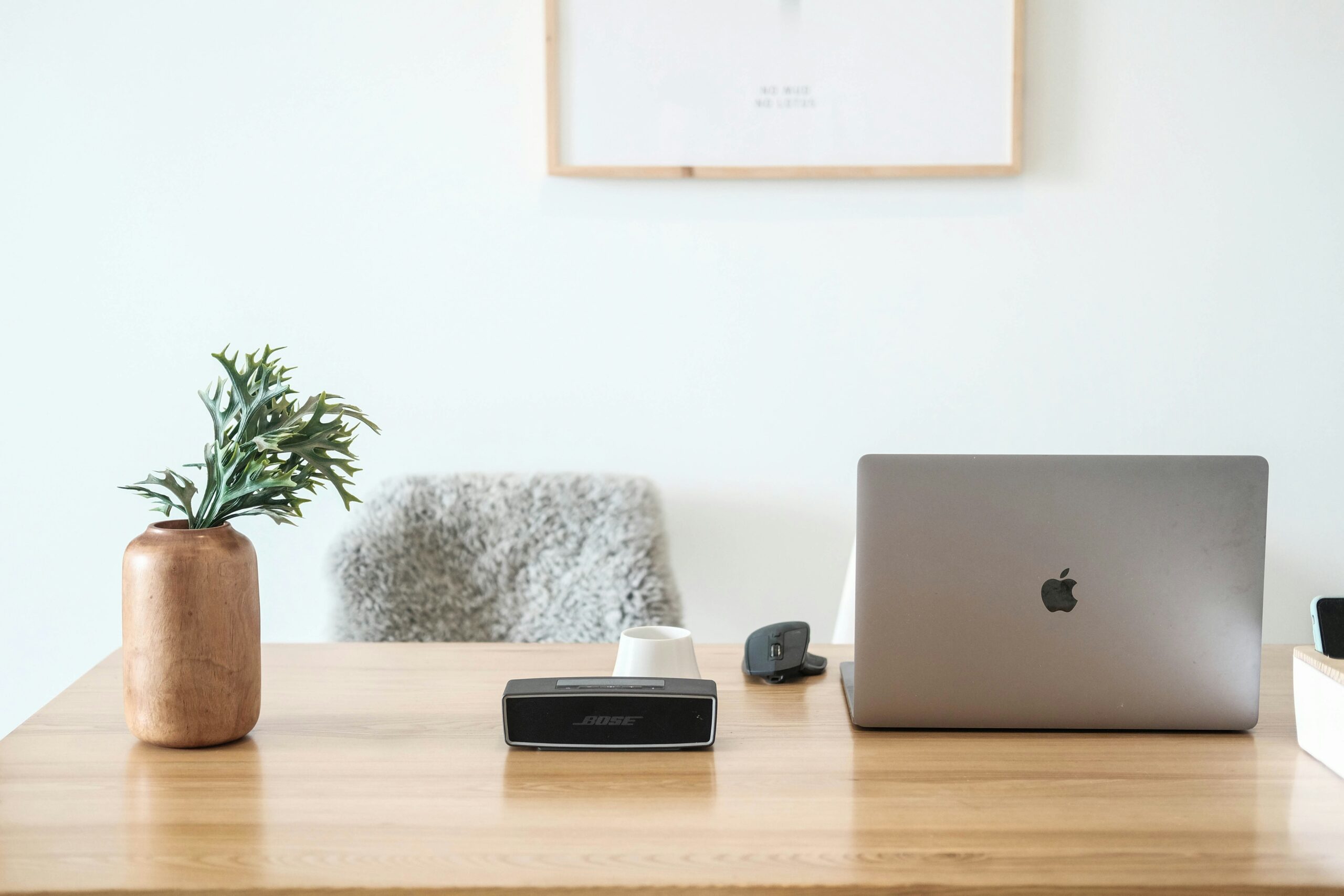 a laptop, speaker, and plant sit on a light wood desk, with a grey chair behind it. used in a blog post about how to build a wedding photography timeline
