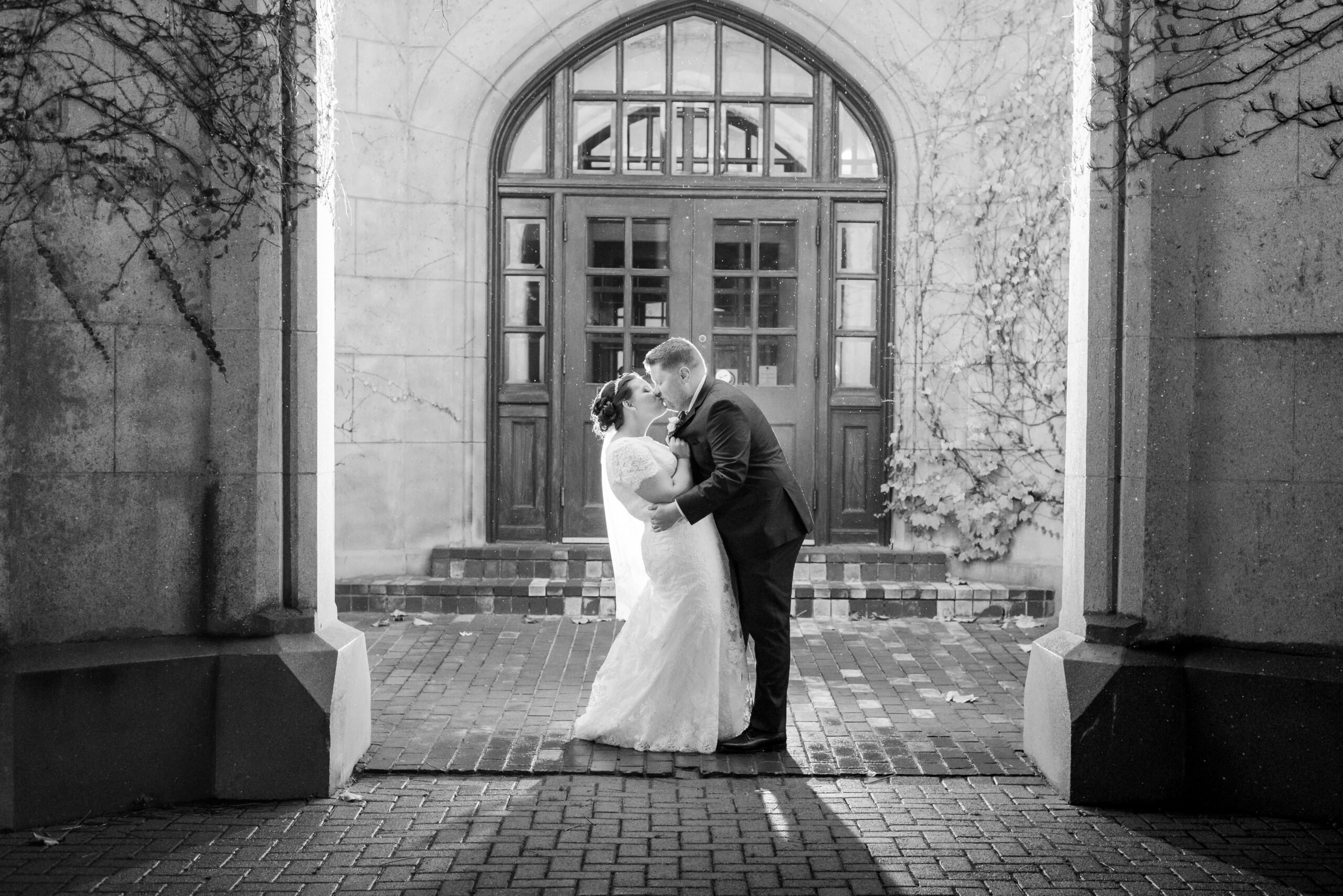 A black and white photo of a bride and groom kissing in front of an old wooden door. Used in a blog post about honeybook workflow setups